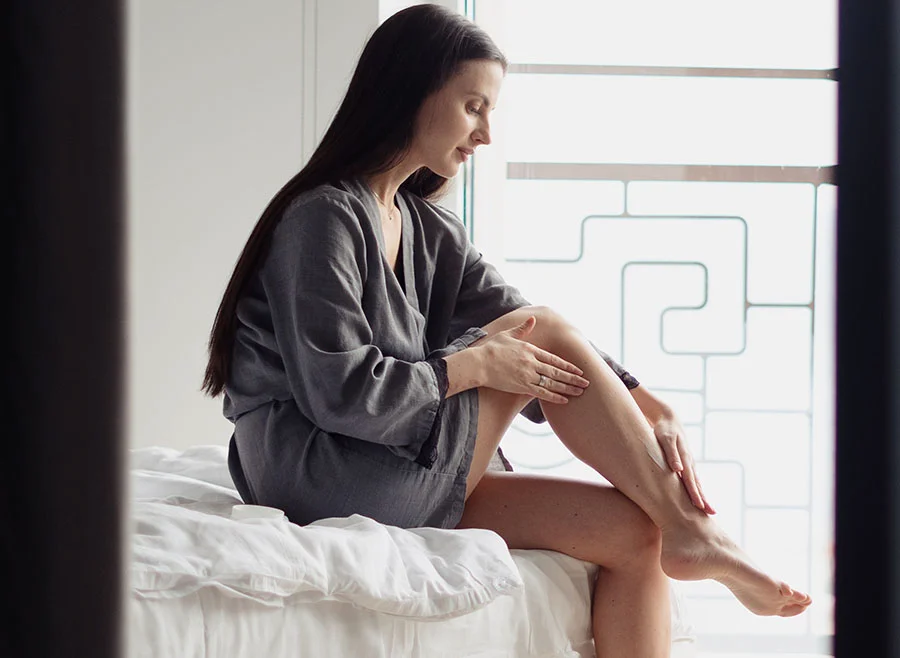 A woman sitting on a bed, gently massaging her leg, with a serene expression - Laser Hair Removal in Chino, CA