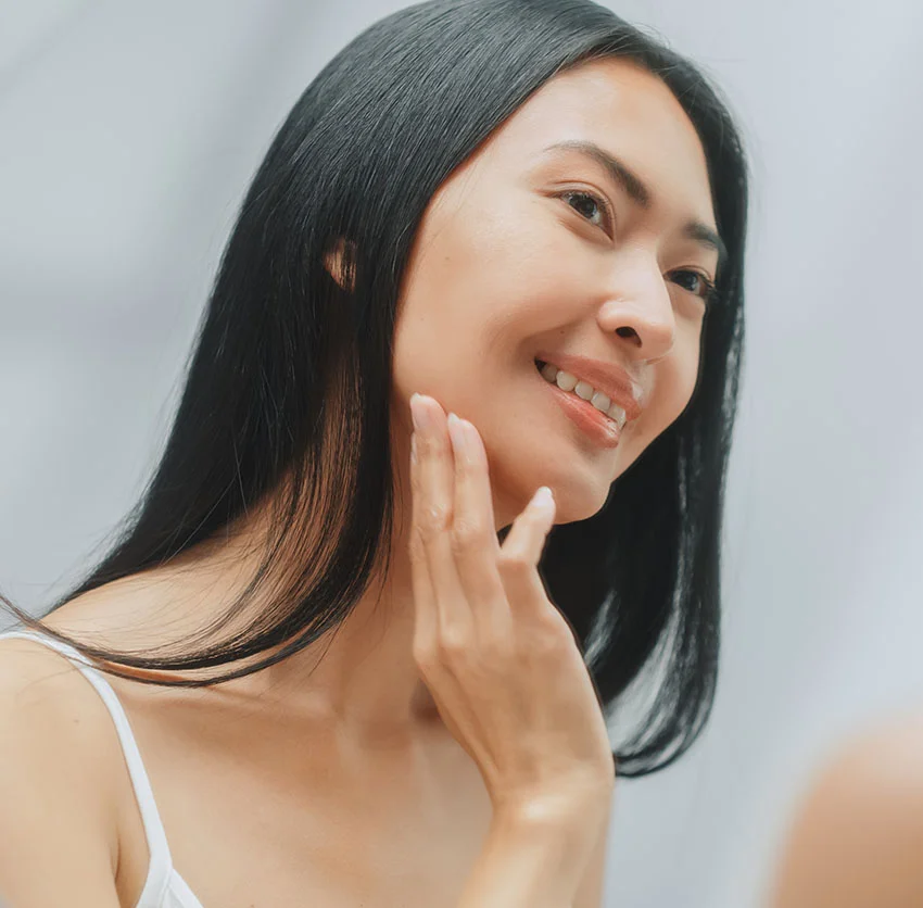 Smiling woman with long black hair and a natural look, gently touching her cheek - Radiesse in Chino, CA