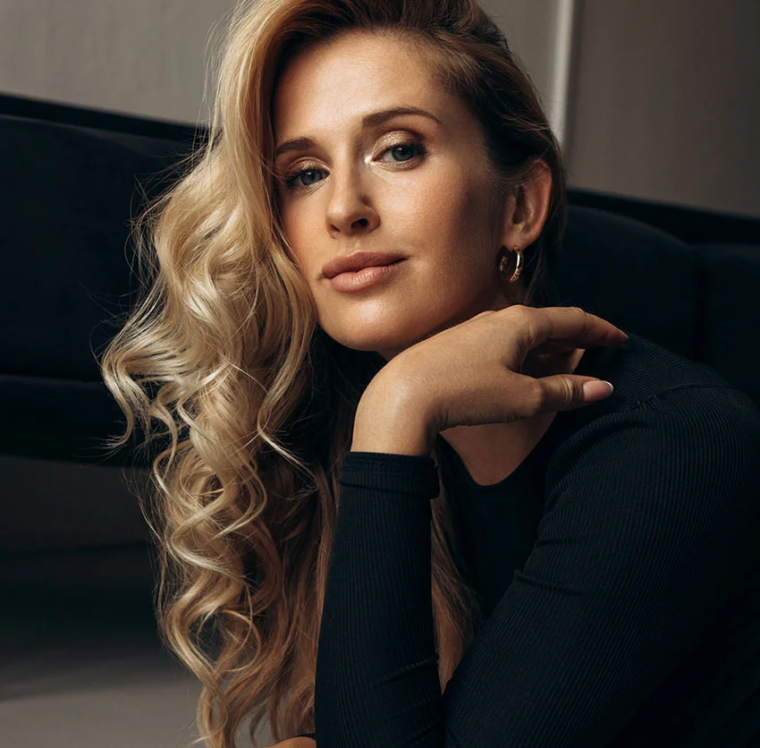 Confident woman with blonde hair styled in loose curls, with her hand raised to her chin - Sculptra in Chino, CA