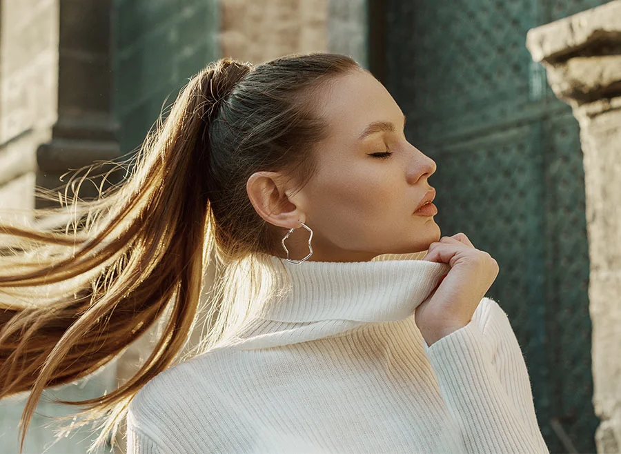 Profile of a woman with long hair pulled back into a ponytail, eyes closed, wearing a white turtleneck sweater - Sculptra in Chino, CA
